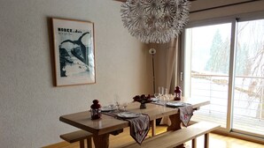 A dining area with a wooden table set for four, a hanging light fixture, and a framed picture on the wall.