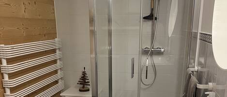 A modern bathroom with a glass shower enclosure, a white sink, and a wooden wall.