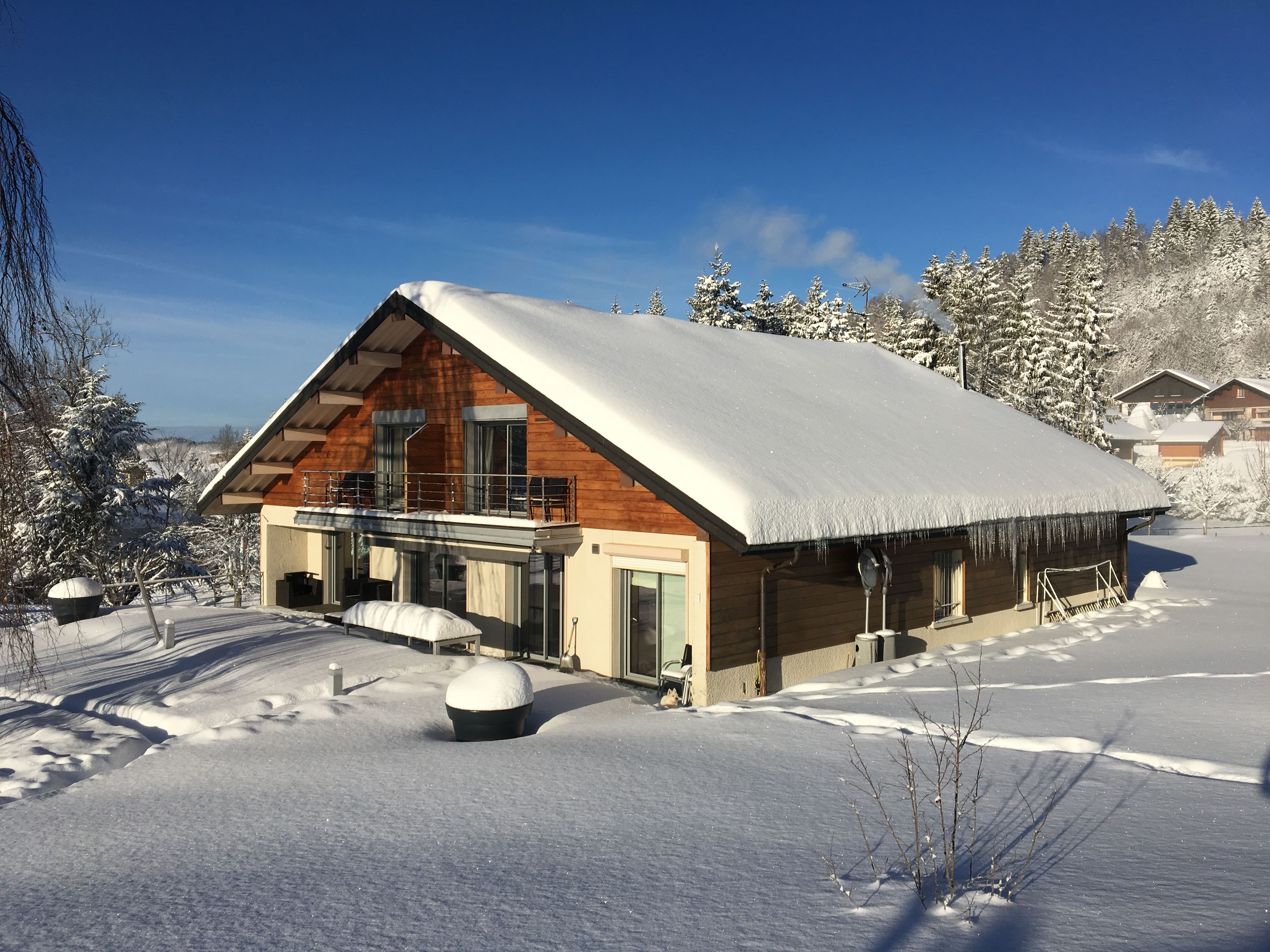 Una cabaña de madera con balcón, rodeada de árboles cubiertos de nieve.