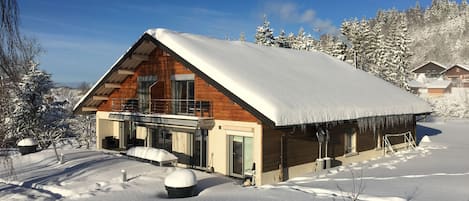 A wooden cabin with a balcony, surrounded by snow-covered trees.