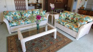 A living room with two wicker sofas, a glass coffee table, and a patterned rug.