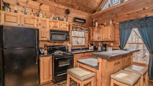 Cocina de cabaña de madera con un refrigerador negro, armarios de madera, microondas, estufa y una zona de bar con taburetes.
