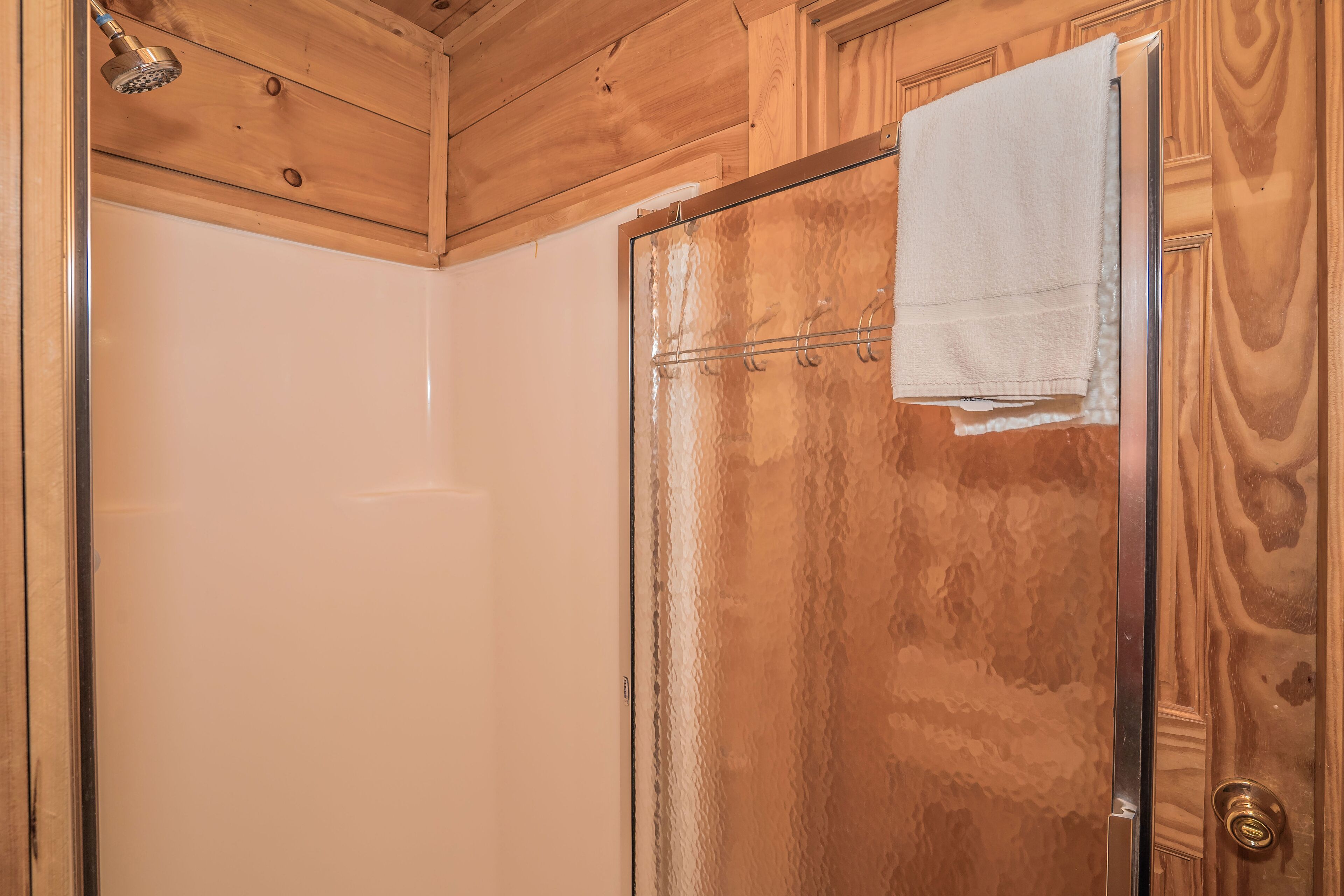 Une cabine de douche en bois avec une porte en verre et une serviette accrochée à la poignée de la porte.