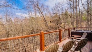 Una terraza de madera con barandilla de metal, dos sillas Adirondack y un jacuzzi.