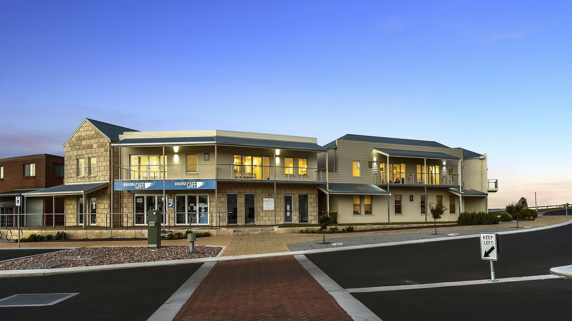 A two-story building with a cafe on the ground floor, a parking sign, and a 'Keep Left' sign at the intersection.