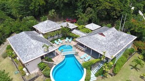 A resort with a central swimming pool, multiple guest rooms, and lush greenery.