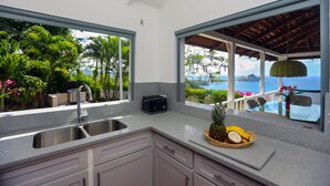 A kitchen with a view of the ocean, a toaster, and a fruit bowl on the counter.