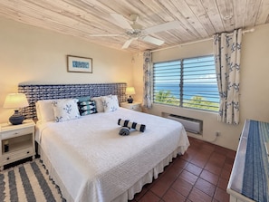 A bedroom with a bed, two bedside tables, a ceiling fan, a window with curtains, and a view of the ocean. - You Won’t Want to Leave, Panoramic Sea Views,  Private Pool,  Caribbean Paradise (Gros Islet)