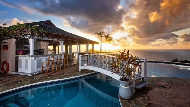 A pool area with a bar, a covered seating area, and a view of the ocean at sunset. - Villa Albatross Nest with Stunning Panoramic Sea View (Gros Islet)