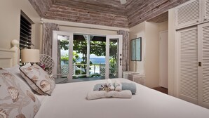 A bedroom with a wooden ceiling, a large bed with white linens, a view of the sea through a glass door, and a white wardrobe. - Villa Albatross Nest with Stunning Panoramic Sea View (Gros Islet)