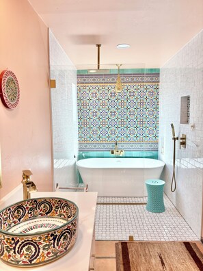 A bathroom with a freestanding bathtub, a sink with a decorative bowl, a shower area, and a patterned tile wall.