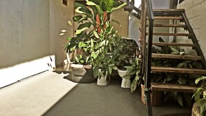 A narrow outdoor corridor with a concrete floor, a wooden staircase, and several potted plants. - Hostel Trotamundos (Alajuela)