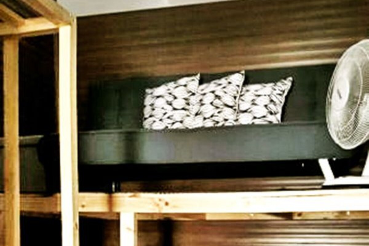 A bunk bed with a ladder, a pillow with a leaf pattern, and a fan on the upper bunk.
