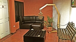 A living room with a black leather sofa, a wooden coffee table, a metal bench, a hanging floor lamp, and a potted plant. - Hostel Trotamundos (Alajuela)