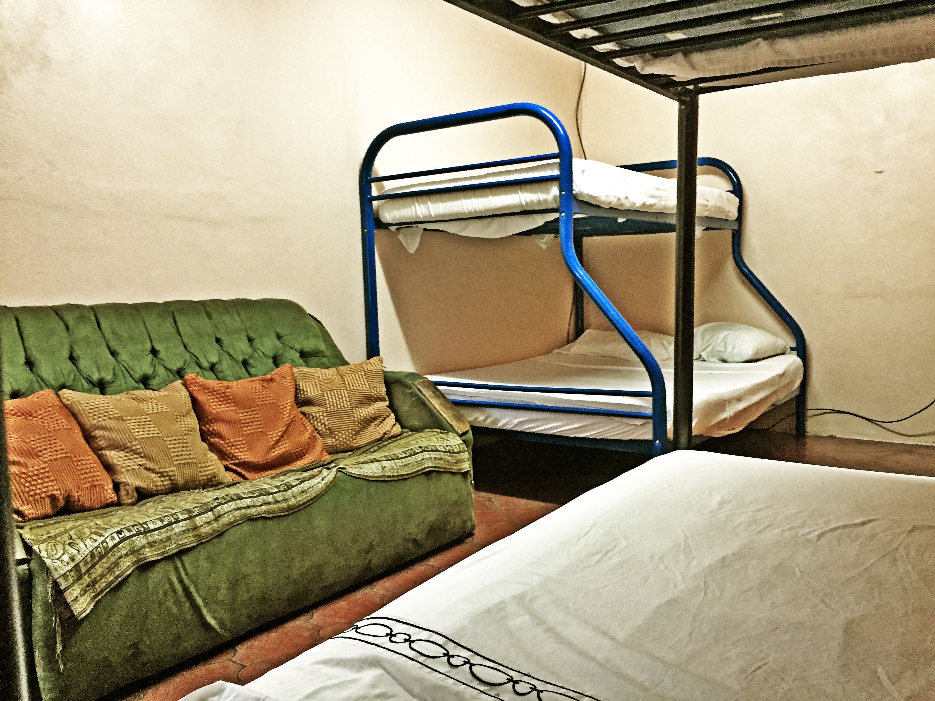 A bunk bed with a green upholstered headboard and pillows, a single bed with white bedding, and a wall socket.