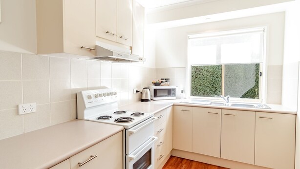 Cocina moderna con armarios blancos, estufa, microondas y ventana con vista a follaje.