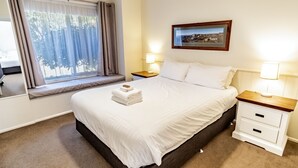 Habitación de hotel con cama, mesitas de noche, ventana con cortinas, un cuadro enmarcado en la pared y una lámpara.