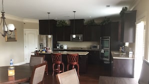 A modern kitchen with dark cabinetry, a central island, and a dining area with wooden chairs and a table. - New Listing! Fully furnished! Available for Master's!! (Augusta)
