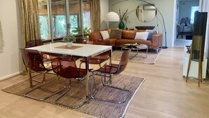 A modern living room with a dining area, featuring a glass table, leather sofa, and a large mirror. - A Great Family Place in Henley Beach - Pets  ✅ opposite park stylish & comfy (Henley Beach)