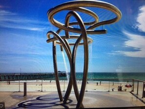 A metal sculpture on a beach with a pier in the background.