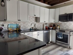 A modern kitchen with white cabinets, a black countertop, stainless steel appliances, and a tiled backsplash. - Wake to Ocean Breezes, End with Stunning Sunsets – Spacious Narragansett Retreat (Narragansett)
