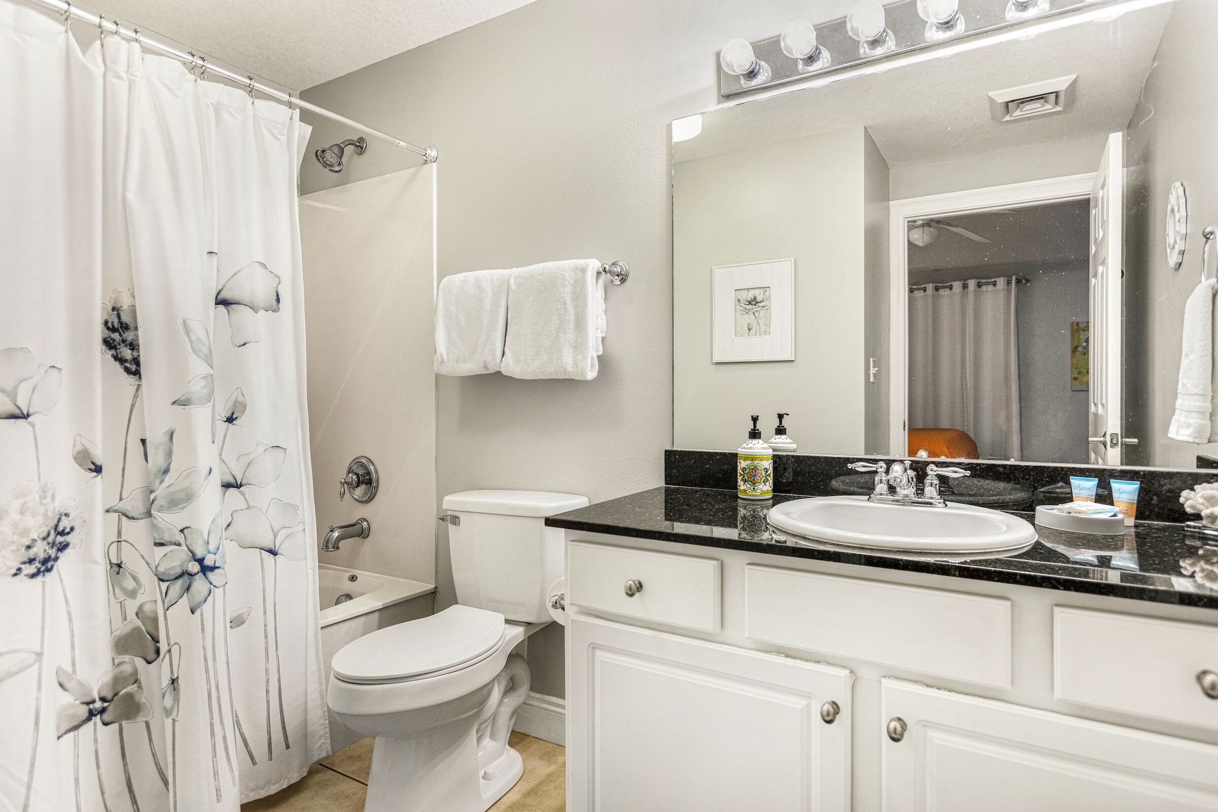 A bathroom with a white toilet, a sink with a black countertop, and a shower curtain with a floral design.