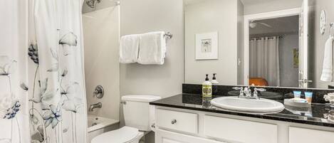 A bathroom with a white toilet, a sink with a black countertop, and a shower curtain with a floral design.
