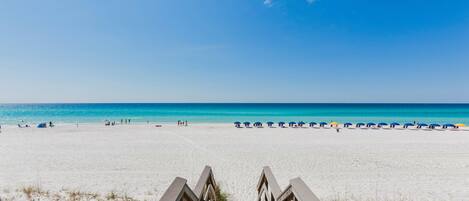 Una spiaggia con una scala di legno che conduce alla sabbia, un cielo azzurro limpido e un mare calmo.