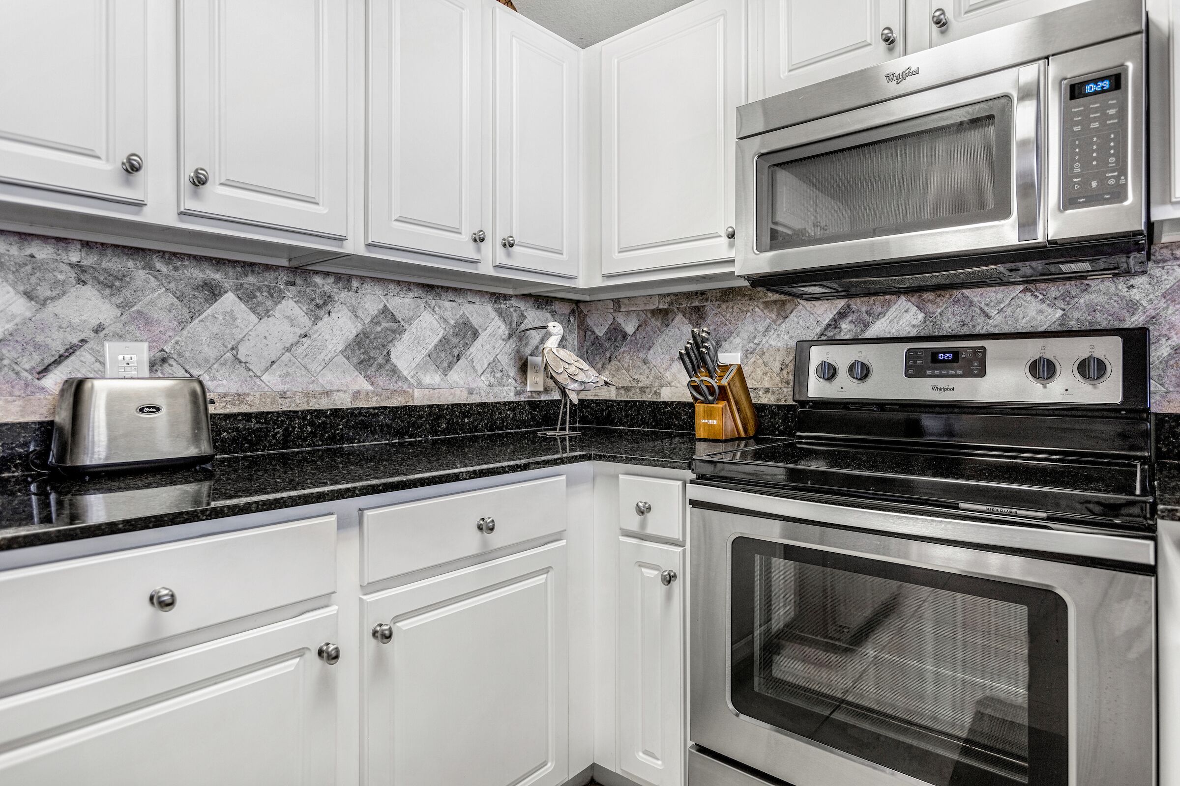 A modern kitchen with white cabinets, a microwave, a toaster, and a stove.