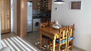 A compact kitchen with a washing machine, wooden cabinets, and a dining table with chairs. - COZY APARTMENT 50 M FROM THE BEACH with WIFI (L'Ampolla)