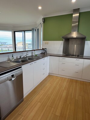 A modern kitchen with a dishwasher, stainless steel range hood, and a view through the window. - Karma Waters Beach House (Middleton)