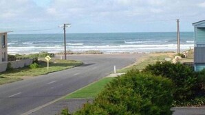 A coastal road with a beach view, a road sign indicating a curve, and a small building on the right.