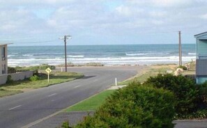 A coastal road with a beach view, a road sign indicating a curve, and a small building on the right.