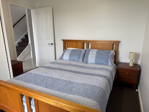 A bedroom with a wooden bed, a nightstand, a lamp, and a door leading to a staircase.