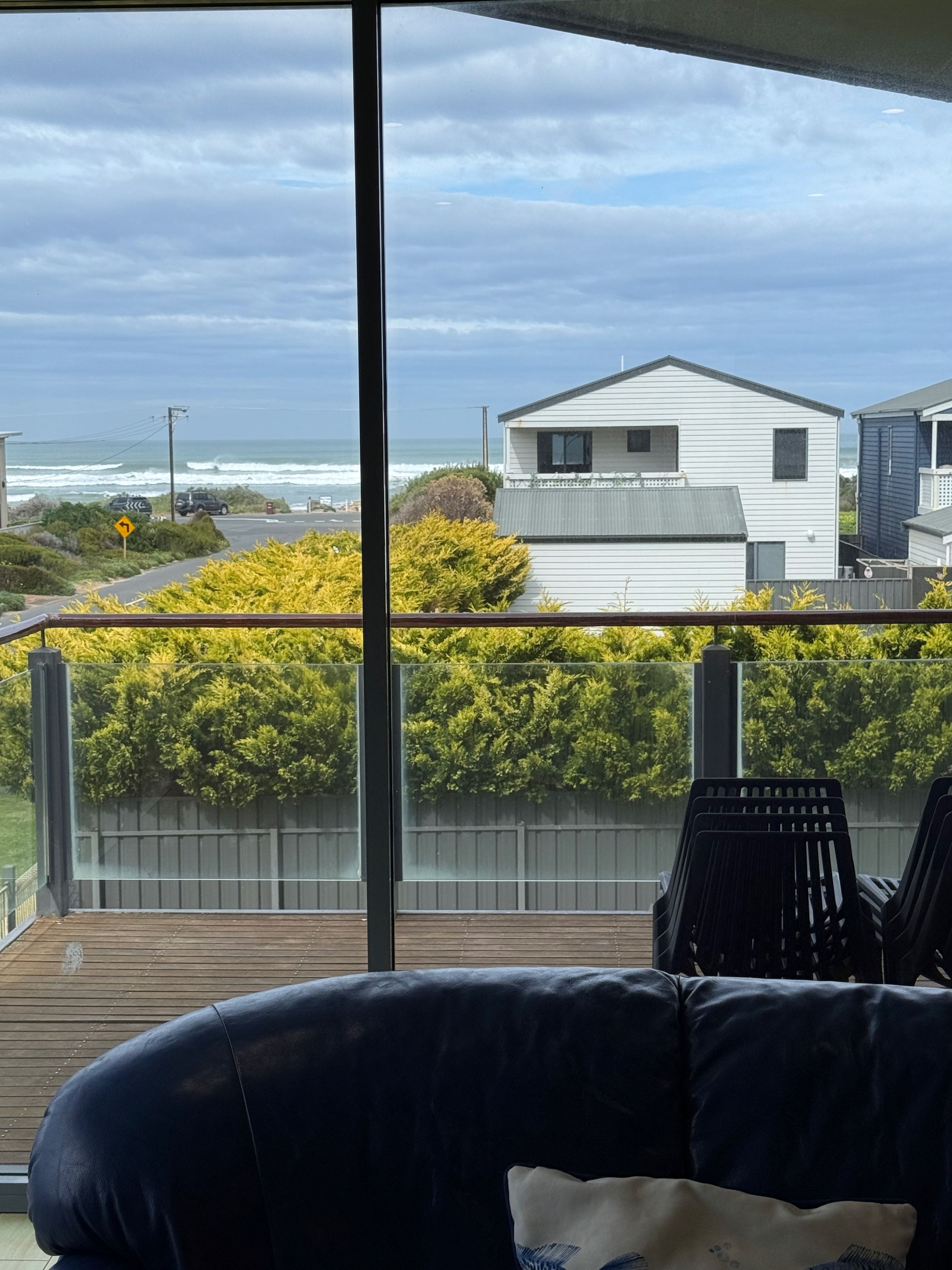 A balcony with a view of a residential area, a wooden deck, and a black leather sofa.