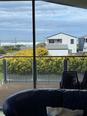A balcony with a view of a residential area, a wooden deck, and a black leather sofa.