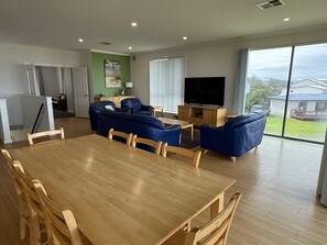 A spacious living area with a wooden dining table, blue sofas, and a flat-screen TV. - Karma Waters Beach House (Middleton)