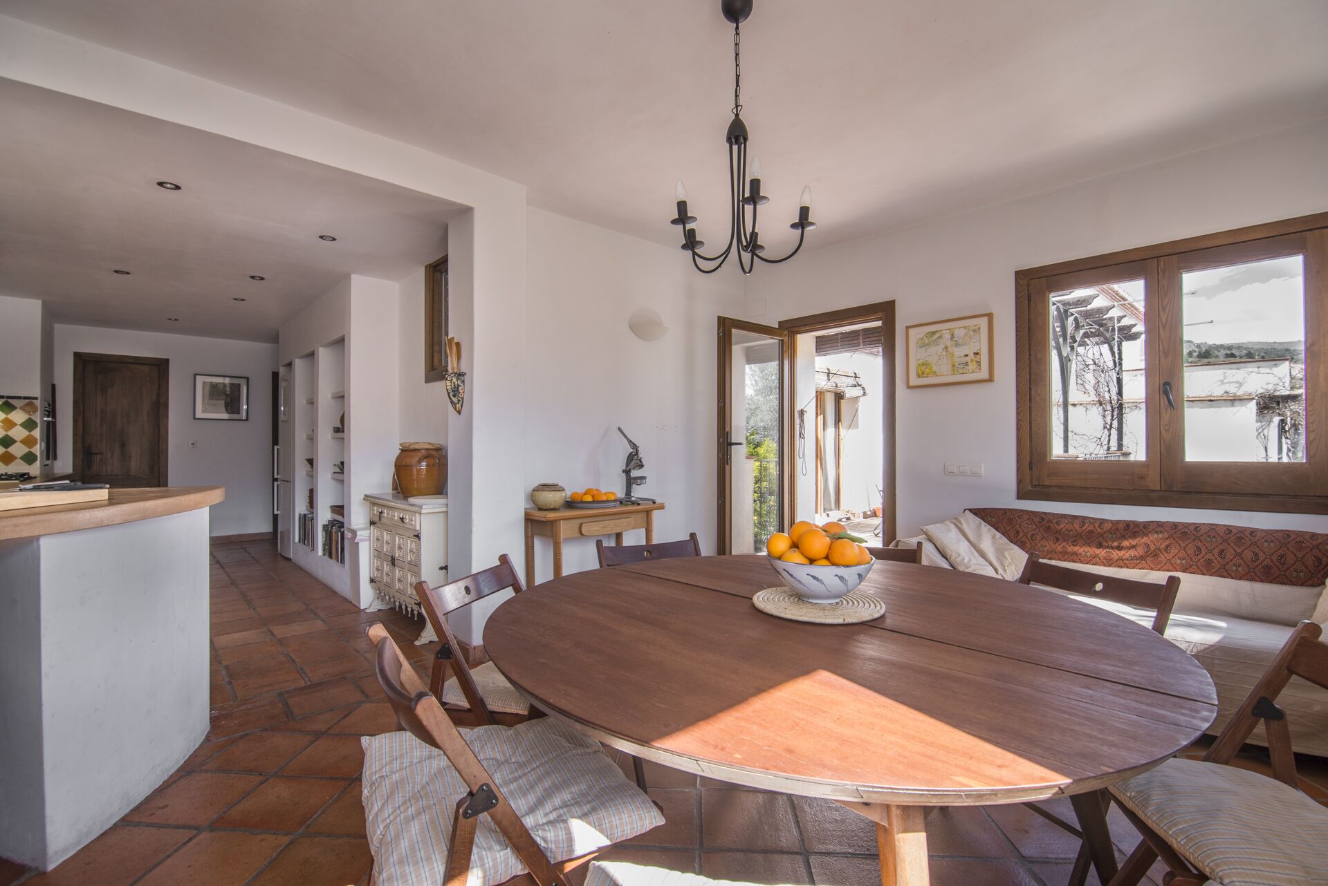 Un comedor con una mesa redonda de madera, sillas, un cuenco de fruta y una araña.