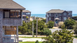 A coastal residential area with two multi-story houses, one with a wooden deck and the other with a balcony, overlooking the beach. - Oceanview Dog Friendly Home w/ Hot Tub, Community Pool and Tennis/Pickleball (Avon)
