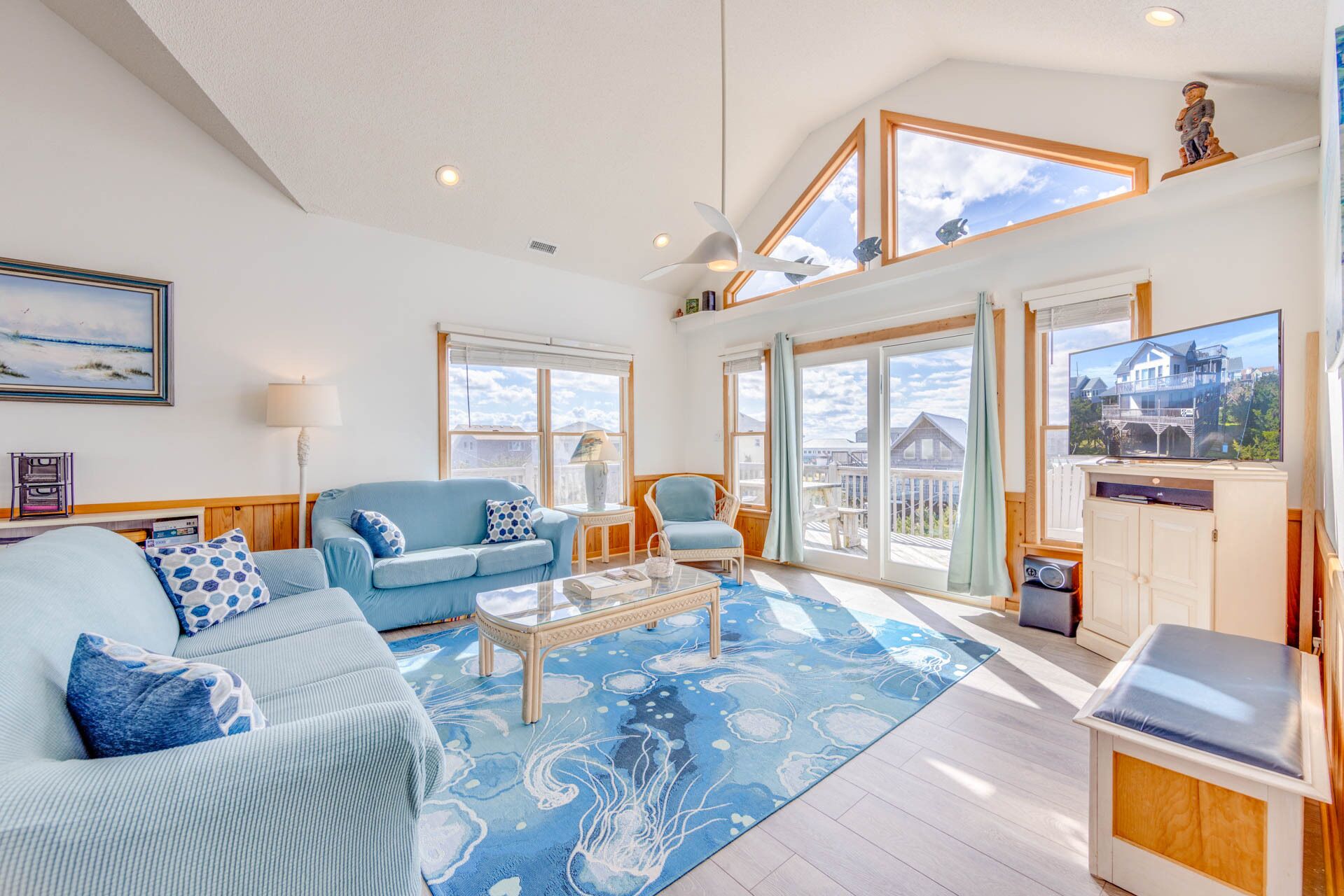A spacious living room with a large window, a blue sofa, a coffee table, and a television.