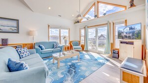 A spacious living room with a large window, a blue sofa, a coffee table, and a television. - Oceanview Dog Friendly Home w/ Hot Tub, Community Pool and Tennis/Pickleball (Avon)