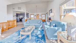 A spacious living room with a large sofa, a glass coffee table, and a patterned rug. There is a kitchen in the background with modern appliances and a dining area. - Oceanview Dog Friendly Home w/ Hot Tub, Community Pool and Tennis/Pickleball (Avon)