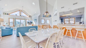 A spacious kitchen with a central island, white dining area with chairs, and a large window overlooking the sea. - Oceanview Dog Friendly Home w/ Hot Tub, Community Pool and Tennis/Pickleball (Avon)