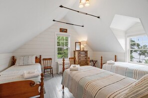 A bedroom with two beds, a dresser, a chair, and a window.