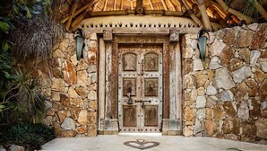 Une façade en pierre avec une porte en bois, un motif en forme de cœur incrusté dans le sol et une toiture en chaume.