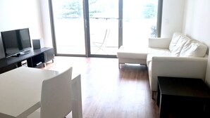 Een moderne woonkamer met een witte bank, een televisie op een zwarte standaard en een eettafel.