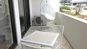 Een balkon met een witte metalen tafel en stoel, een hangstoel, en een kleine tuin met planten en een boom.