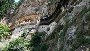 Un bâtiment en pierre doté de balcons et d’un escalier en bois, situé au bord d’une falaise.