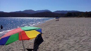 Une plage avec un parasol aux couleurs vives, une eau d’un bleu limpide et des montagnes en arrière-plan.