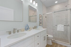 Features a sleek countertop, two sinks, and a large mirror, along with a glass-enclosed shower and a toilet.